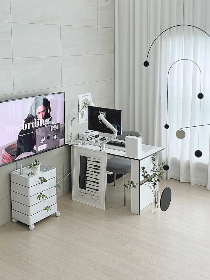 白を基調としたリビングタイプのホームオフィス、モニターアーム付きのデスクとトロリー収納が配置されたシンプルな印象的な空間