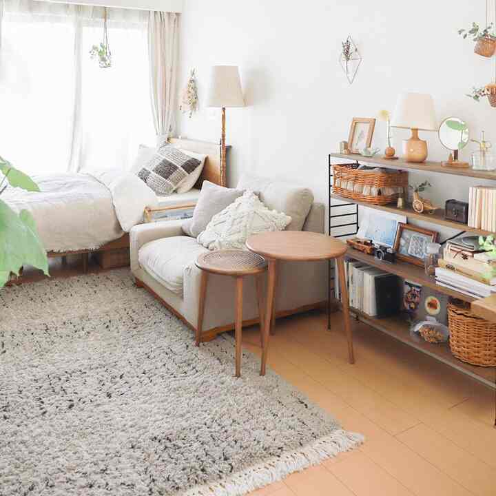 Bright and airy white and beige studio apartment living room featuring low beige sofa and wooden side tables with cozy atmosphere