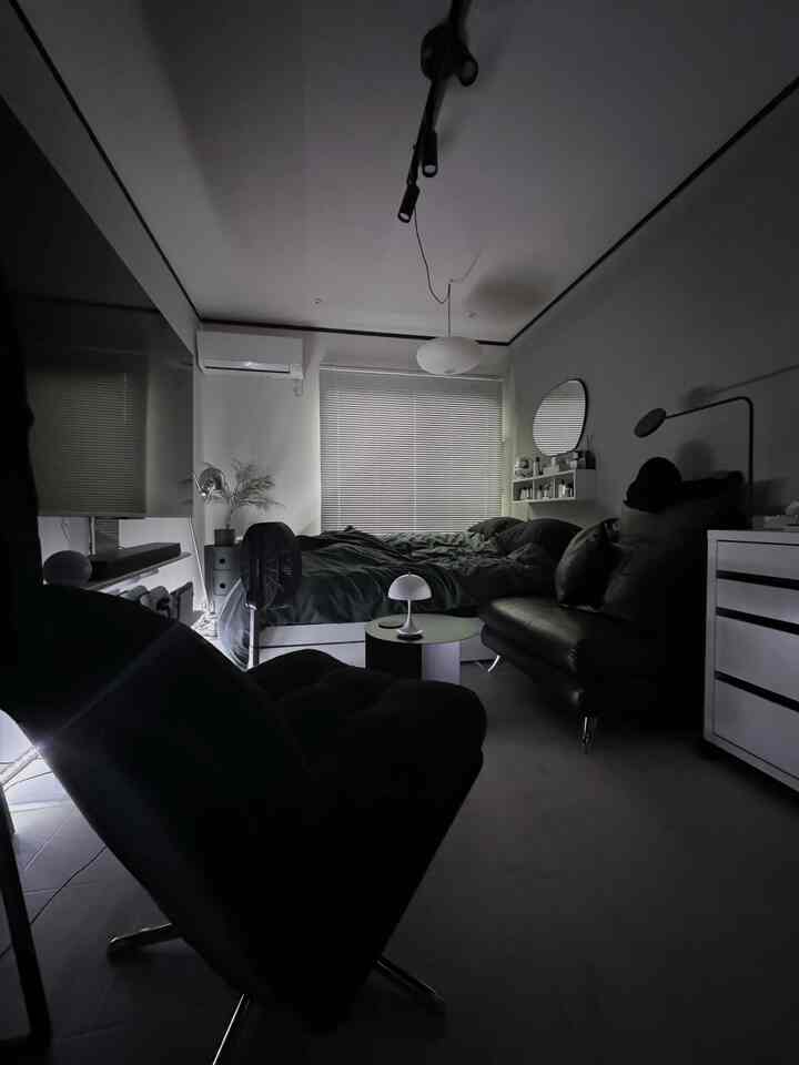 Black and white toned bedroom featuring a large central bed and armchairs in the foreground with a modern atmosphere