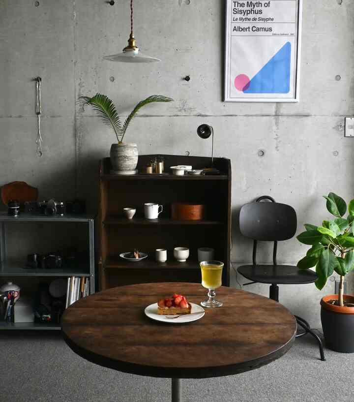 グレーのコンクリート壁とヴィンテージ木製テーブル、椅子、棚が配置されたナチュラルでモダンなインテリア