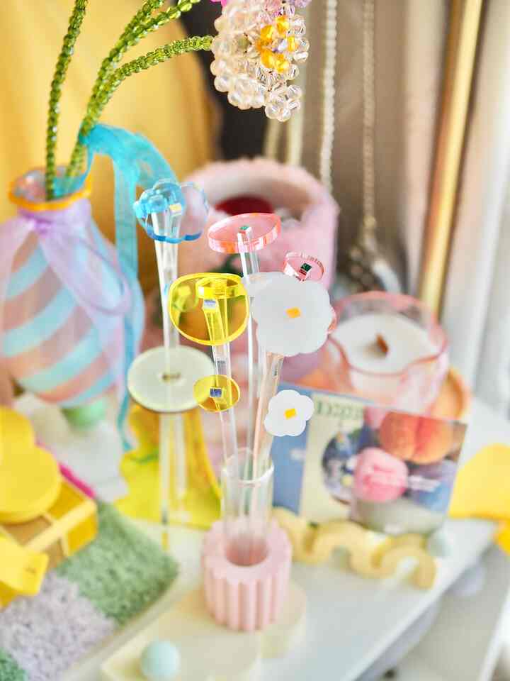 A yellow-toned table featuring transparent acrylic vases with colorful acrylic flower decorations in a bright, cheerful interior.