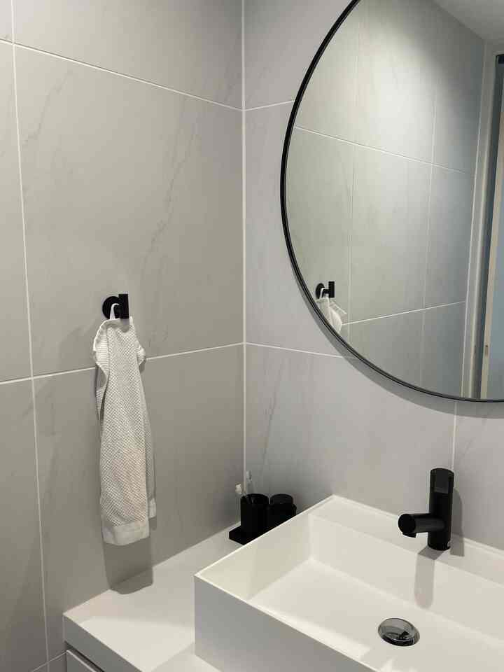 モノトーン調でシンプルなデザインのバスルーム、黒の水栓と丸い鏡が配置された洗面空間