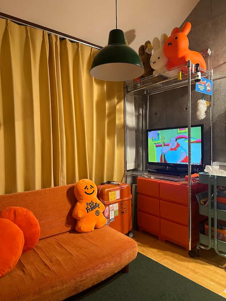 温かみのあるオレンジ色調のリビング、中央に緑のペンダントライトがあり、オレンジのソファと収納が配された印象的な空間