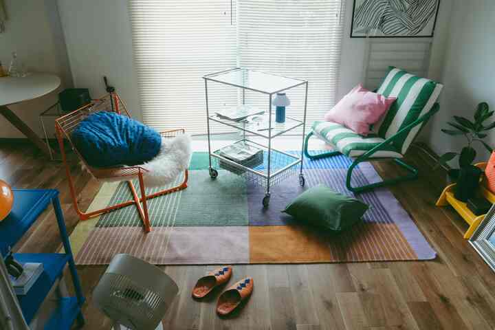A compact living room with natural tones and diverse colors, featuring two chairs and a colorful rug in a modern setting