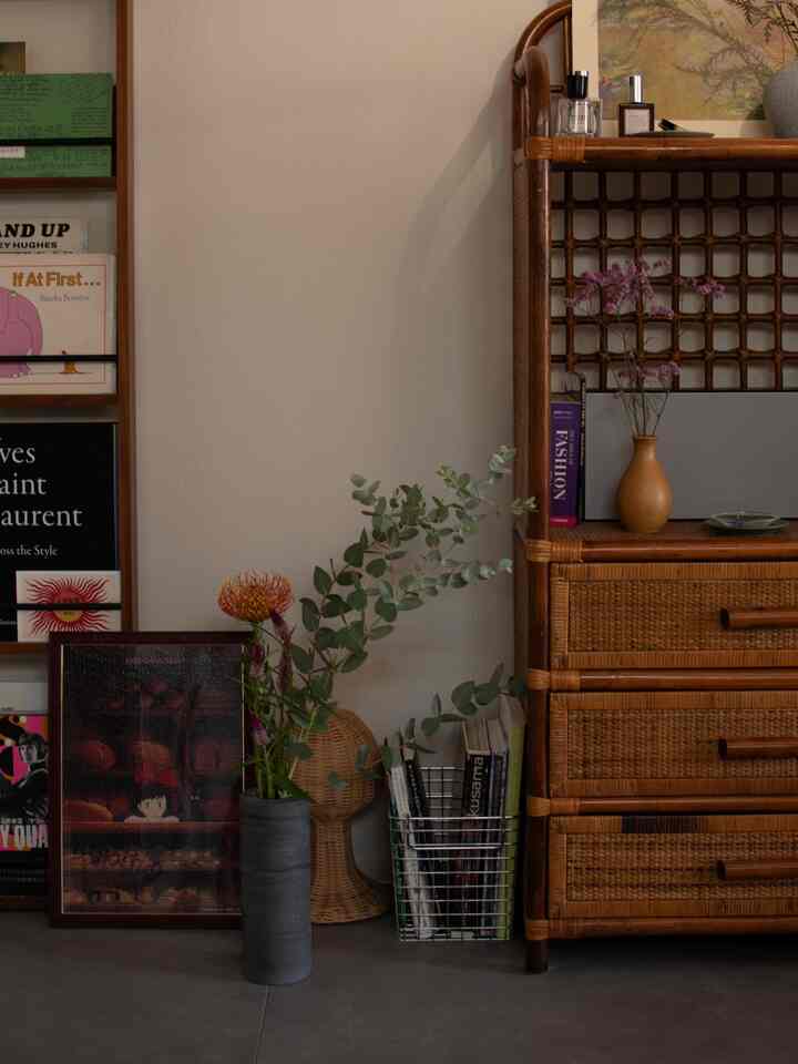 ベージュの壁と茶色のラタン家具があるワンルーム、花瓶と植物、額装されたアートが配置された雰囲気のあるインテリア