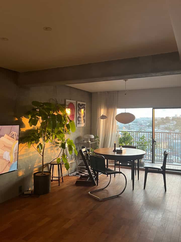 Wood tone and black mid-century modern living room featuring a round dining table, plants, and natural light from balcony windows