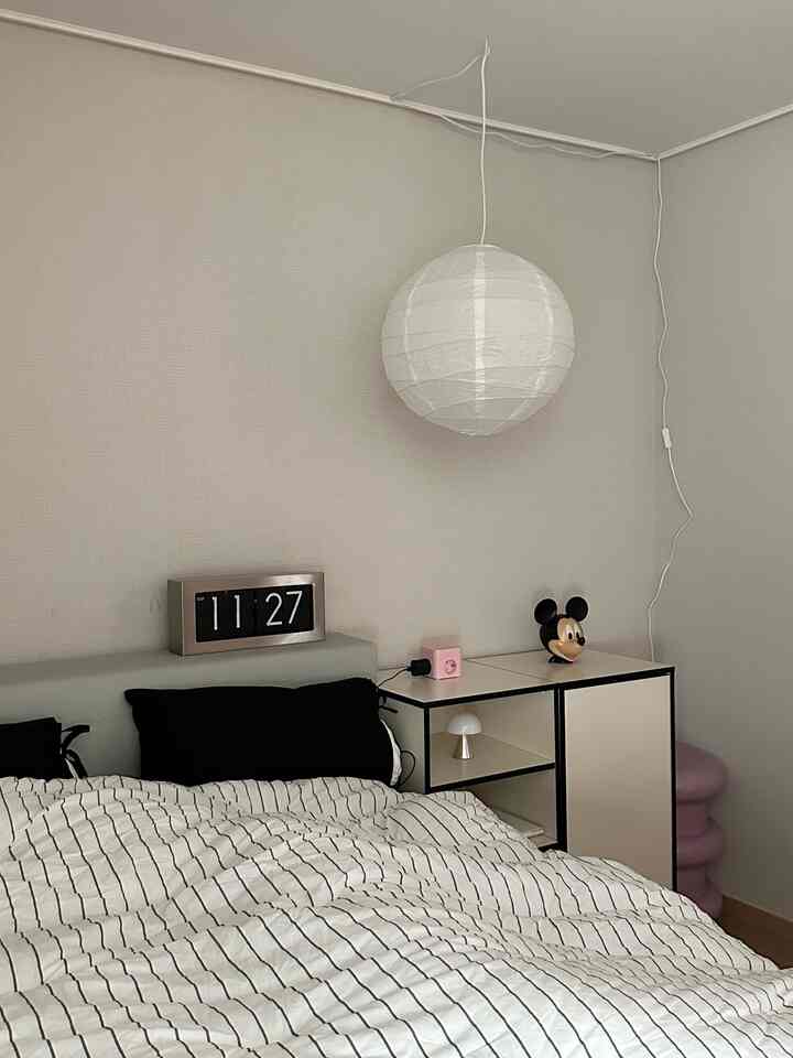 Bright white and beige toned bedroom featuring a pendant light and digital clock with a simple atmosphere