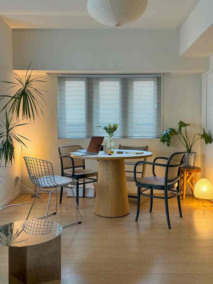 白い壁と木目調の床のダイニング、丸テーブルとアームチェア、植物が配置されたモダンで落ち着いた空間