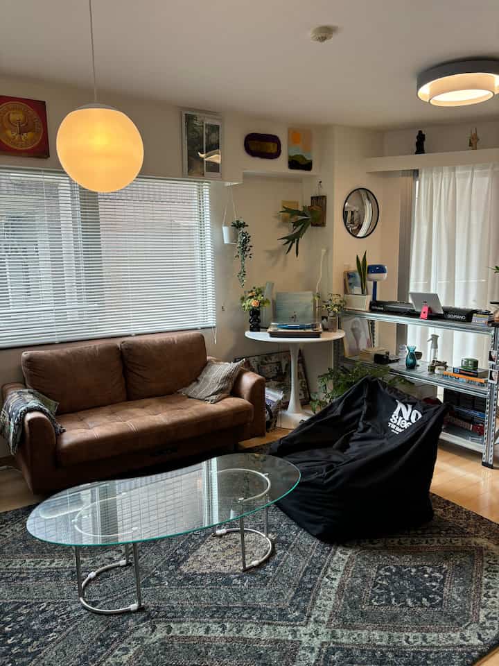Natural tones vintage living room featuring a brown leather sofa, glass coffee table, and various plants with cozy atmosphere
