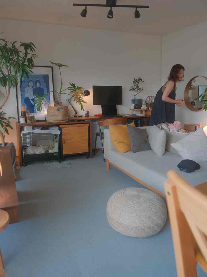 ベージュとグレーの色調のリビング、ソファとスツール、デスクに鏡や植物が配置された雰囲気のあるナチュラルなインテリア