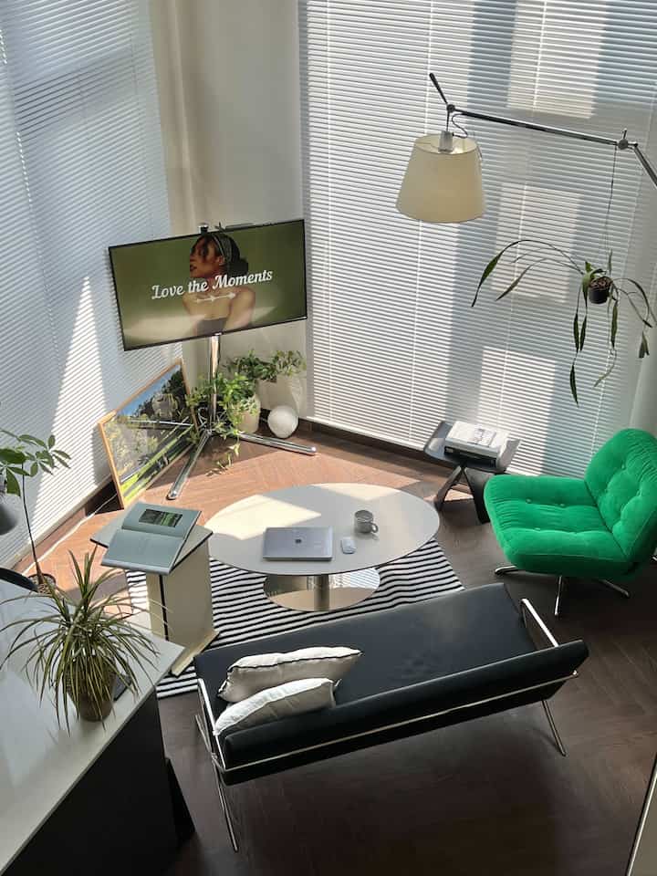 白色のリビングルーム、ブラインドと緑のアームチェア、黒いソファと植物が配置されたモダンで自然な雰囲気のインテリア