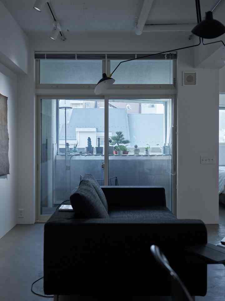 Modern living room in white tones featuring a black sofa and floor lamp with visible balcony through windows