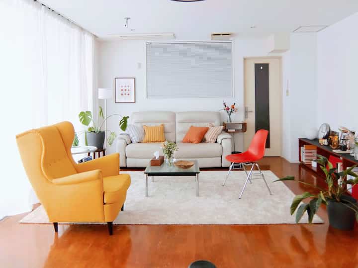 白を基調とした背景に、黄色のアームチェアと赤い椅子が配置されたミッドセンチュリーモダンなリビングの印象的な空間