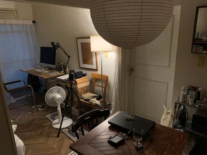 ブラウンとホワイトのトーンのアパートの小さな部屋、デスクやフロアランプなどの家具が配置された散らかった在宅勤務スペース