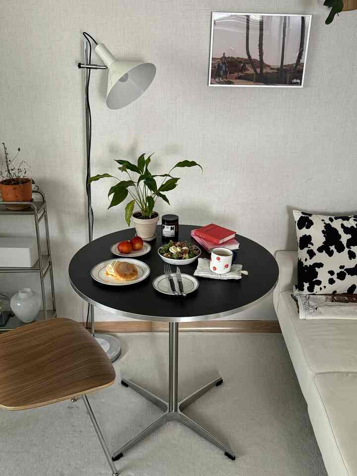 ホワイトとブラックのトーンのワンルームダイニング空間、円形テーブルとソファ、フロアランプが配置されたナチュラルモダンなホームカフェの雰囲気