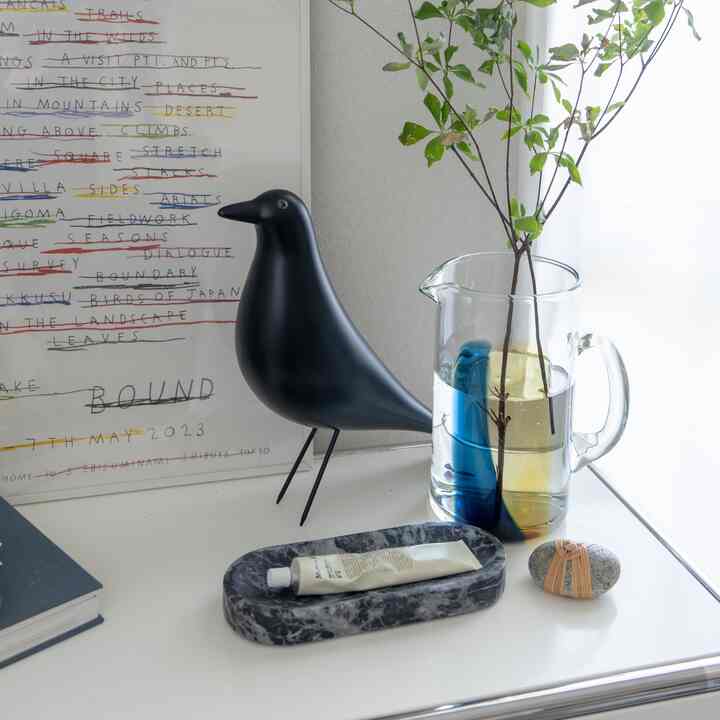 白を基調とした背景に透明なガラスのピッチャーと緑の枝、黒い鳥のオブジェが配置されたシンプルでナチュラルモダンなインテリア