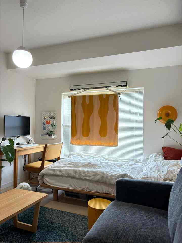 明るいナチュラルカラーの一人暮らし1K寝室、北欧家具とオレンジ色のブランケットが配置された雰囲気のあるインテリア