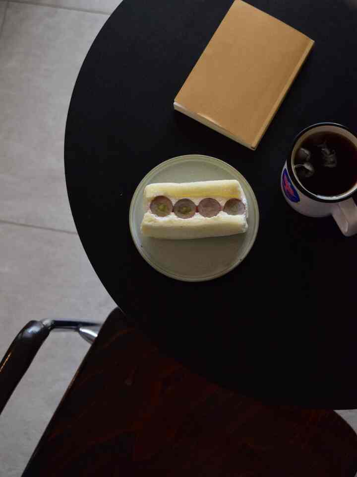 チャコール色の丸いコーヒーテーブルにデザートプレート、本、マグカップが配置された雰囲気のある空間