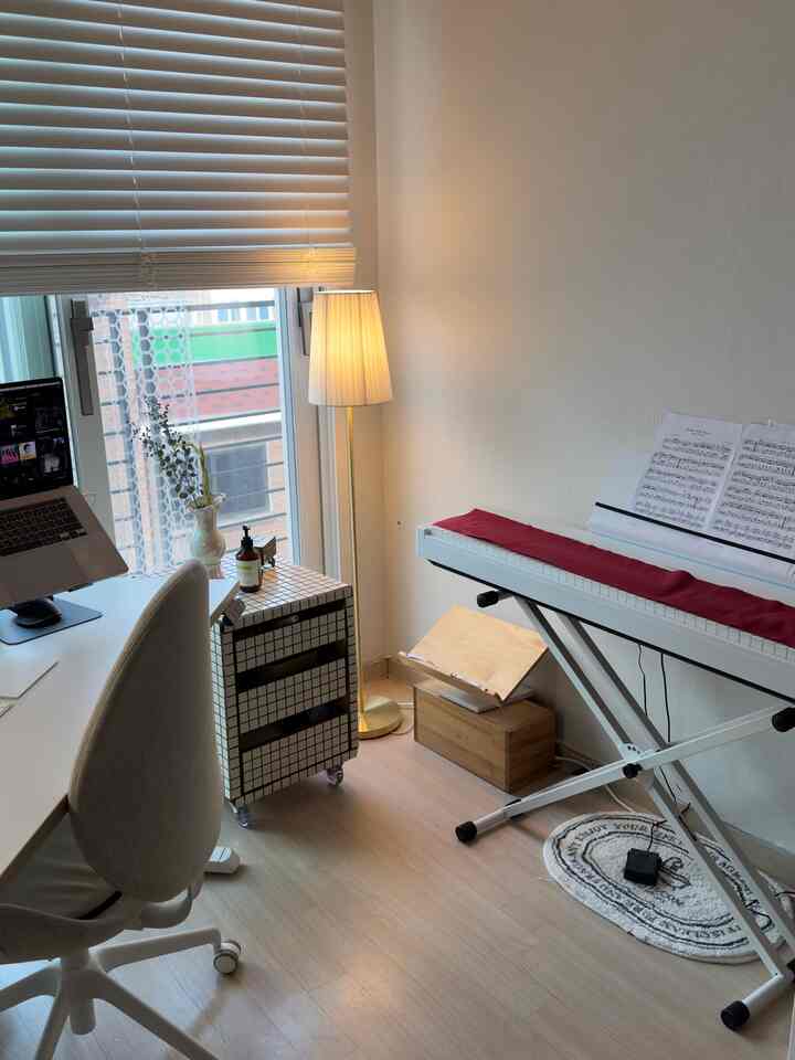 白と木目調が調和したホームオフィス兼作業スペース、電子ピアノとフロアランプが配置された落ち着いた印象の空間