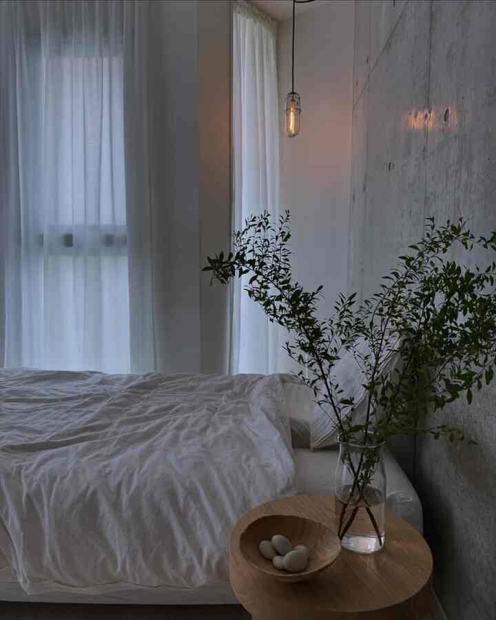 白とナチュラルカラーのトーンの寝室、透明な花瓶と木製ナイトテーブルが配置されたシンプルで自然な雰囲気のインテリア