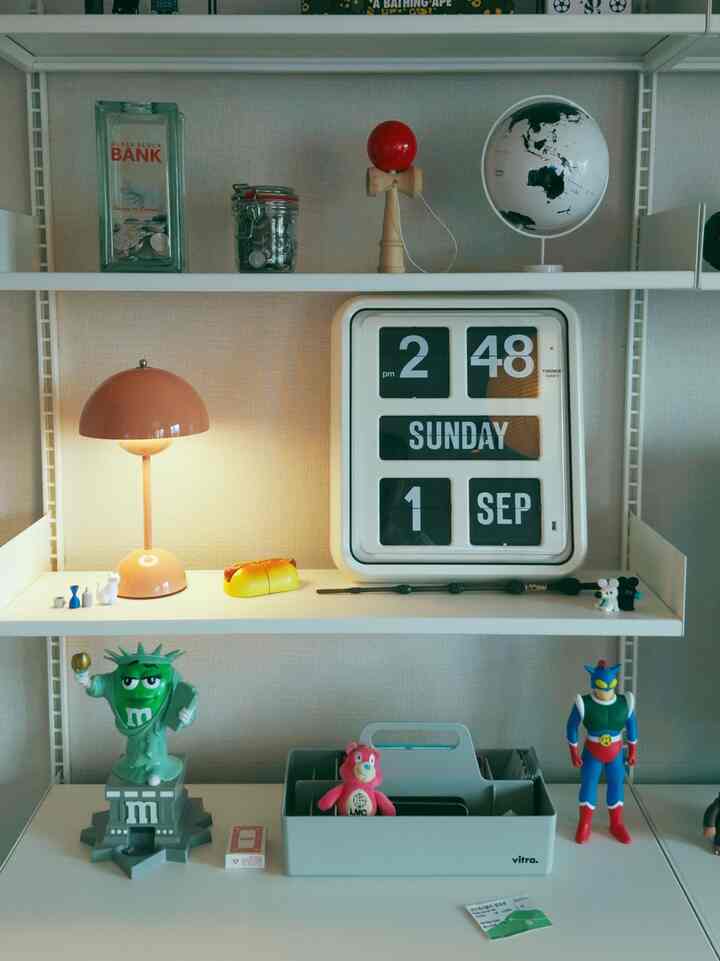 White and gray toned living room shelves featuring a pink table lamp, flip clock, and mid-century modern decor items against a beige wall