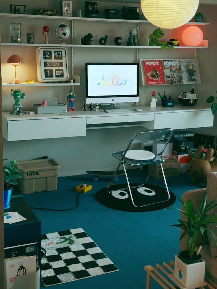 A simple home office space with a white wall-mounted desk and blue carpet, shelves filled with books and decorative accessories