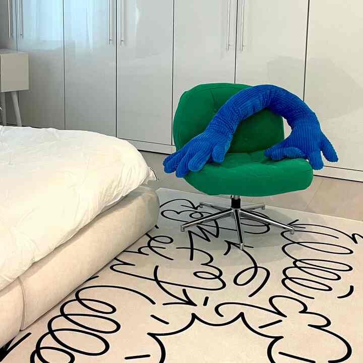 白い壁とベッド、グリーンのアームチェアに青いクッションが配されたミッドセンチュリーモダンな寝室の印象的な空間