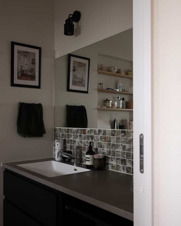 Modern powder room with natural tones featuring black lower cabinets, gray countertop, large mirror, and tiled backsplash creating a sleek atmosphere