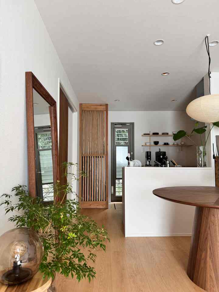 ブラウンの木目調と白い壁のモダンダイニング、丸テーブルと大きな鏡が配置された落ち着いた空間