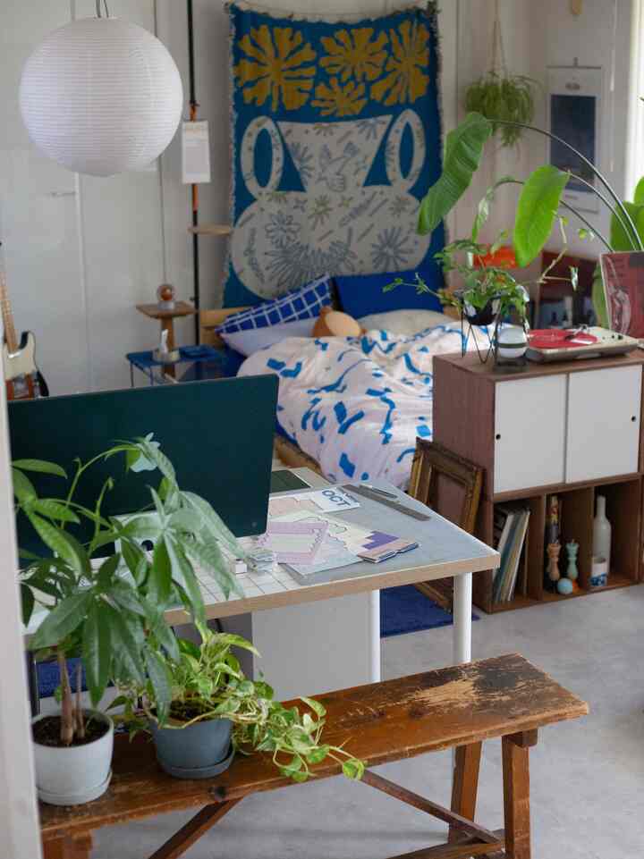 白い壁と青いファブリックが調和する寝室、机と収納棚が配置された自然で落ち着いた雰囲気のインテリア