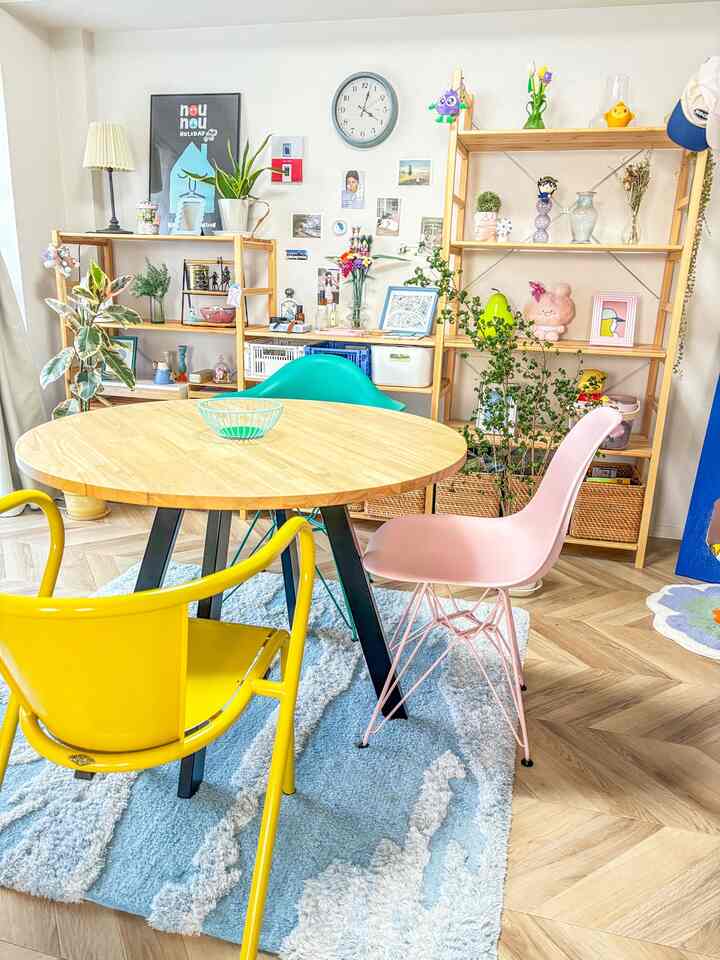 明るい木目調のリビング兼ダイニング空間、丸いダイニングテーブルとカラフルな椅子が配置された雰囲気のあるインテリア