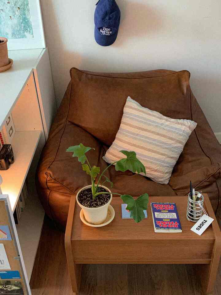 ブラウンのビーズクッションソファと植物が置かれたサイドテーブルのある温かみのあるリビングスペース