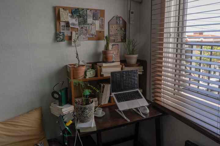 ウッドトーンとベージュの寝室兼ホームオフィス空間、デスク上にノートパソコンと植物が配置され、温かみのある秋らしい雰囲気のインテリア