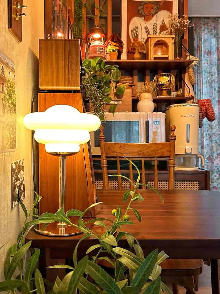 Cozy kitchen space with warm brown tones featuring wooden dining table and chairs, table lamp, and plants in a vintage-style interior