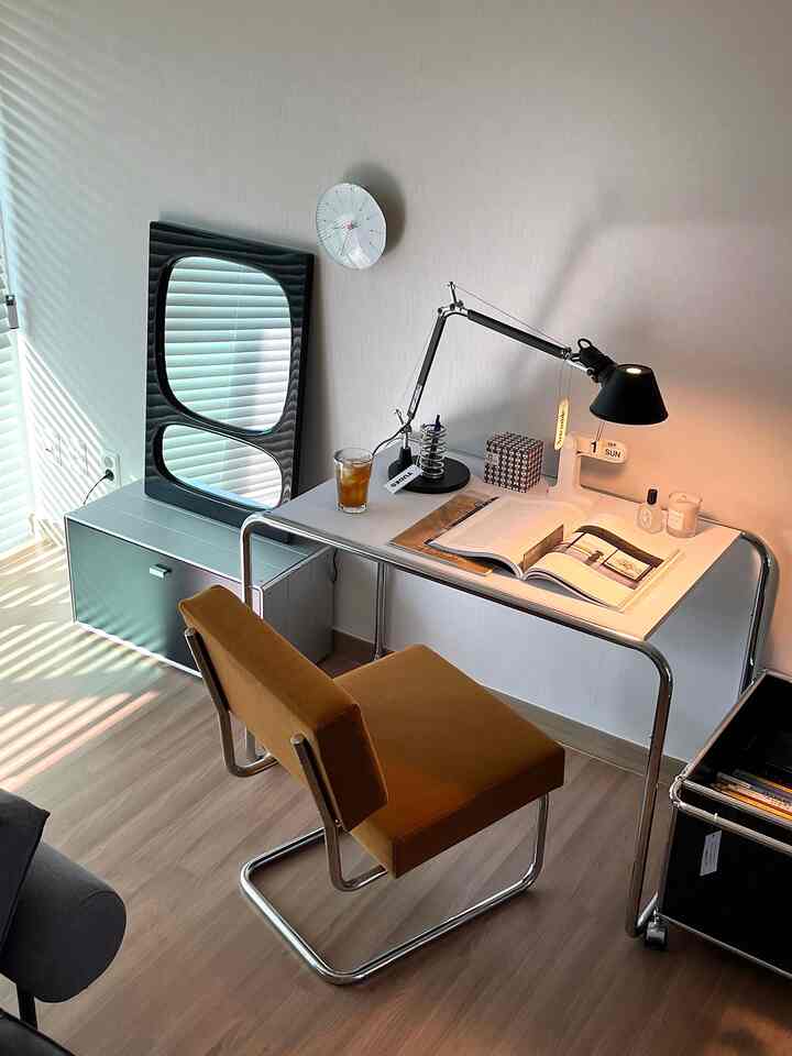 白い壁と茶色の床のミッドセンチュリーモダン書斎、クロームフレームのデスクと茶色い椅子が配置された印象的な空間