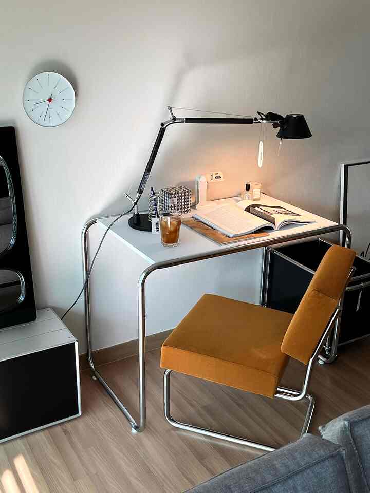白と茶色のトーンのホームオフィス、モダンな金属フレームのデスクとテーブルランプ、オレンジの椅子が配置された印象的なインテリア