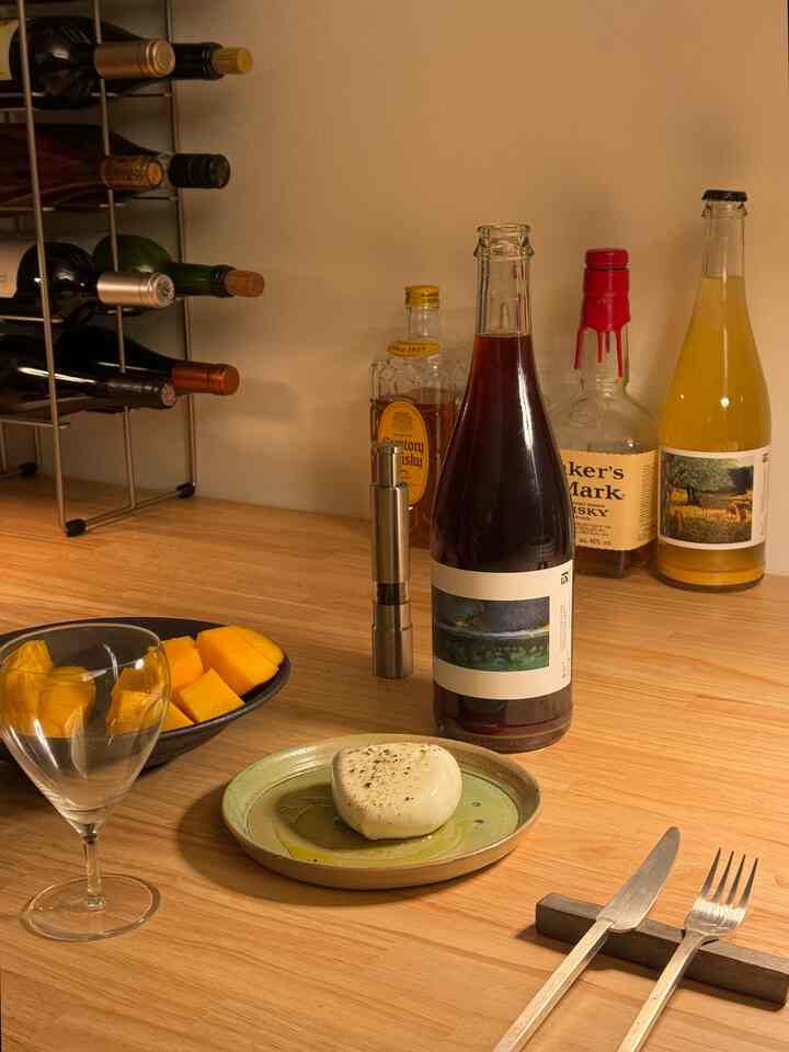 暖かみのある茶色の木製テーブル、ワインボトルと純銅のカトラリーが配置された一人暮らしのキッチンの雰囲気ある空間