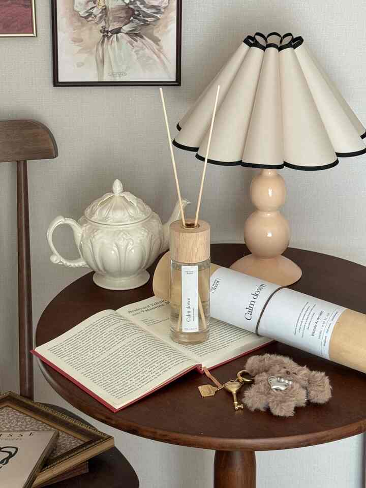 ナチュラルな木目調の丸いナイトテーブルにディフューザーとテーブルランプ、ヴィンテージ小物が置かれた印象的なリビング