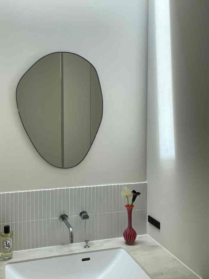 White-toned bathroom with an irregular mirror and sleek sink area, creating a clean space
