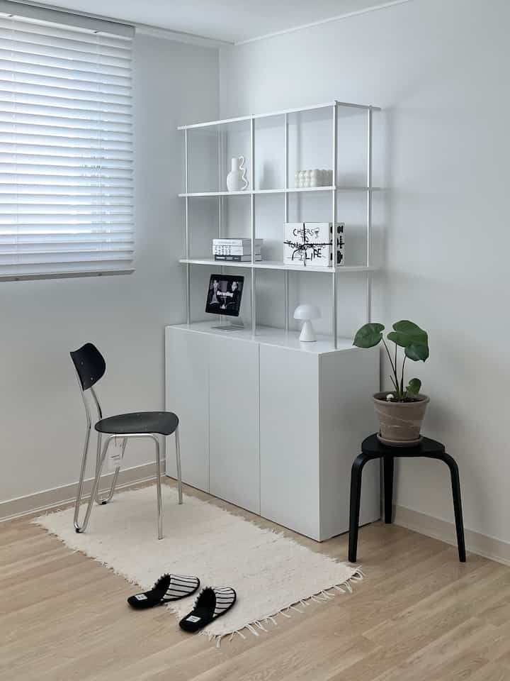 ホワイトとナチュラルトーンのミニマルな小さなリビング空間、棚、椅子、植物、ラグが調和した印象的なインテリア