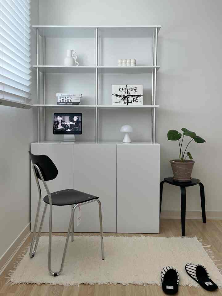 白と木目調が調和したワンルーム、シンプルなキャビネットと棚に植物と小物が配置されたミニマルなインテリア