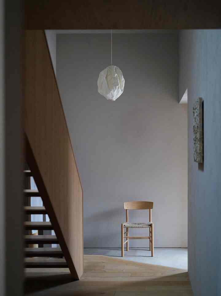 Natural-toned entrance featuring a wooden chair and staircase, creating a simple and serene space