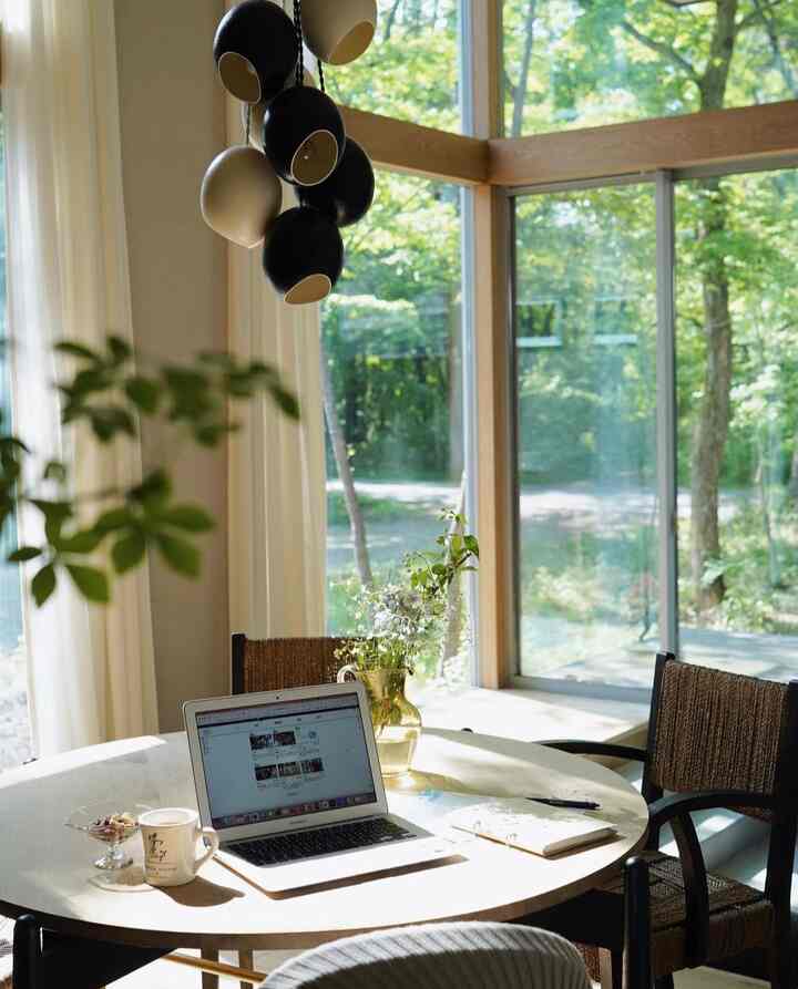 Light brown and white toned living room featuring a round dining table and armchairs, large windows with natural light creating a natural work space
