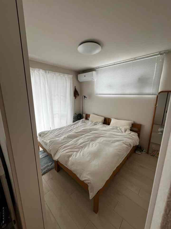 白と木目調の2人用寝室、並んで配置されたオーク製ベッドフレームと明るいブラインドがある印象的な空間