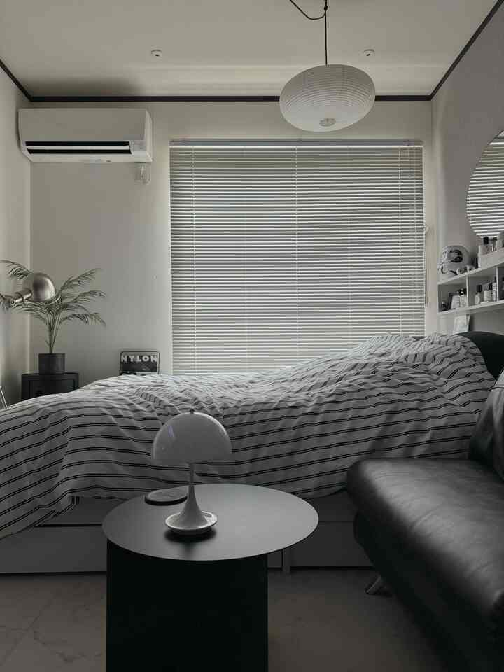 White and black toned single household bedroom featuring striped bedding, blinds, and minimalist table lamp in a modern space