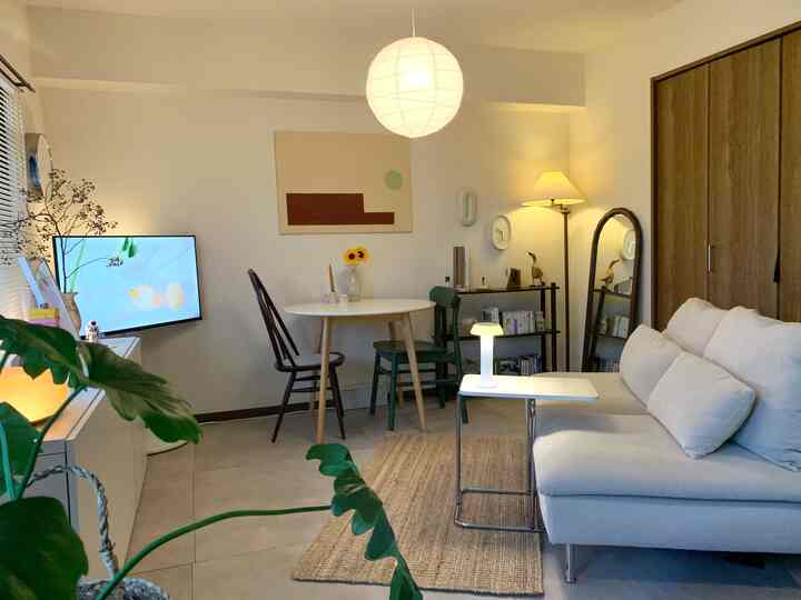 White and natural color toned living room featuring a sofa, round dining table, and plants with a cozy, neat atmosphere