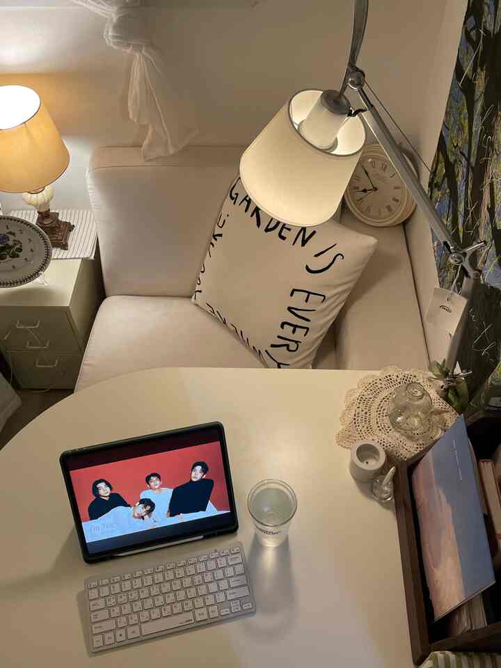 White-toned compact living space featuring a sofa, table with tablet and keyboard, table lamps, and cushions creating a cozy atmosphere