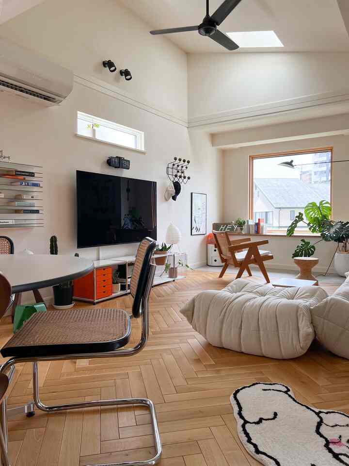 Modern living room with white walls and wood-tone herringbone floor, featuring armchair by window and low sofa cushions in bright and cozy atmosphere