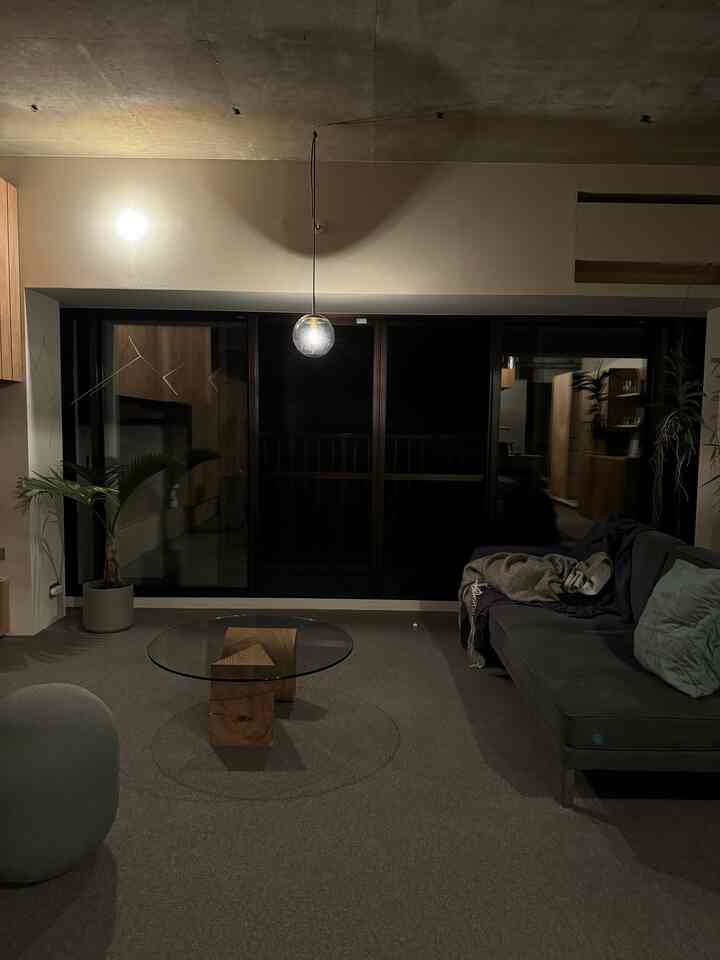 落ち着いたナチュラルトーンのリビング、グレーのソファと木目調家具、ガラステーブルが配置された雰囲気のある空間