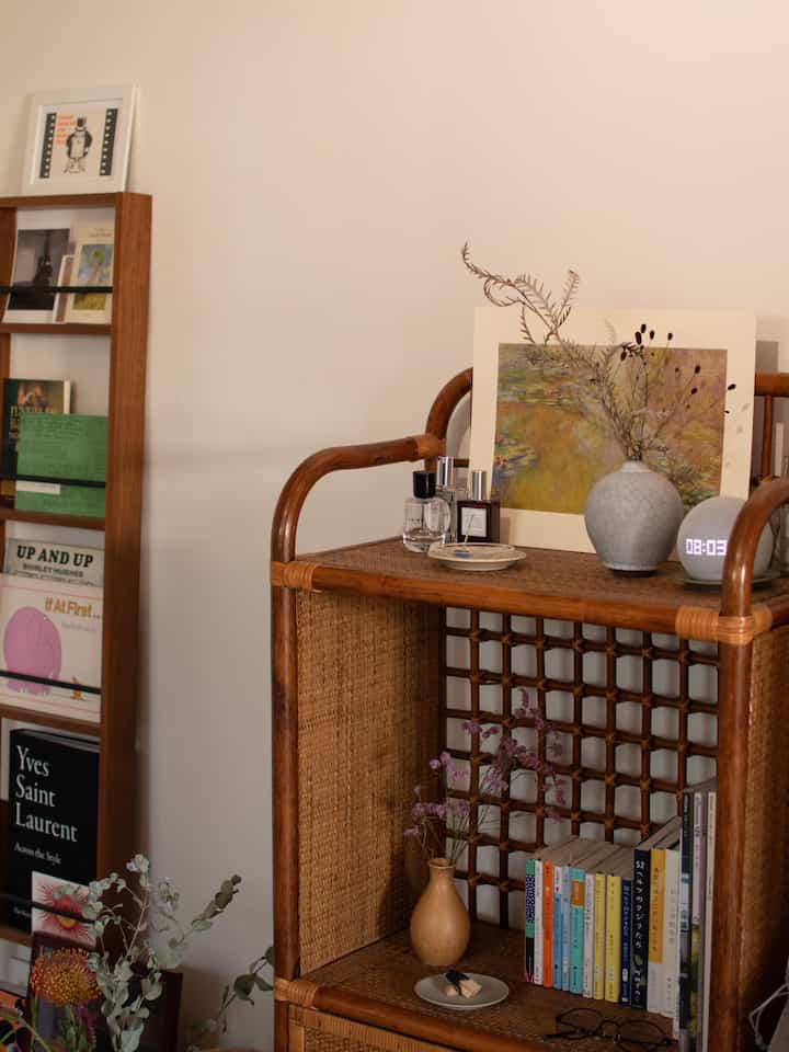 ナチュラルカラーのワンルーム、ラタンのキャビネットと本棚が配置されたシンプルで温かみのある雰囲気のインテリア